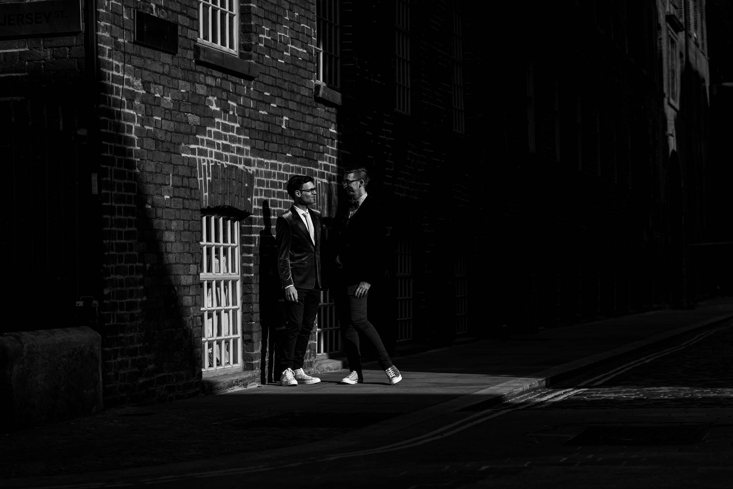 Mono photo of the two grooms stood in a shaft of sunlight in Manchester's northern quarter.