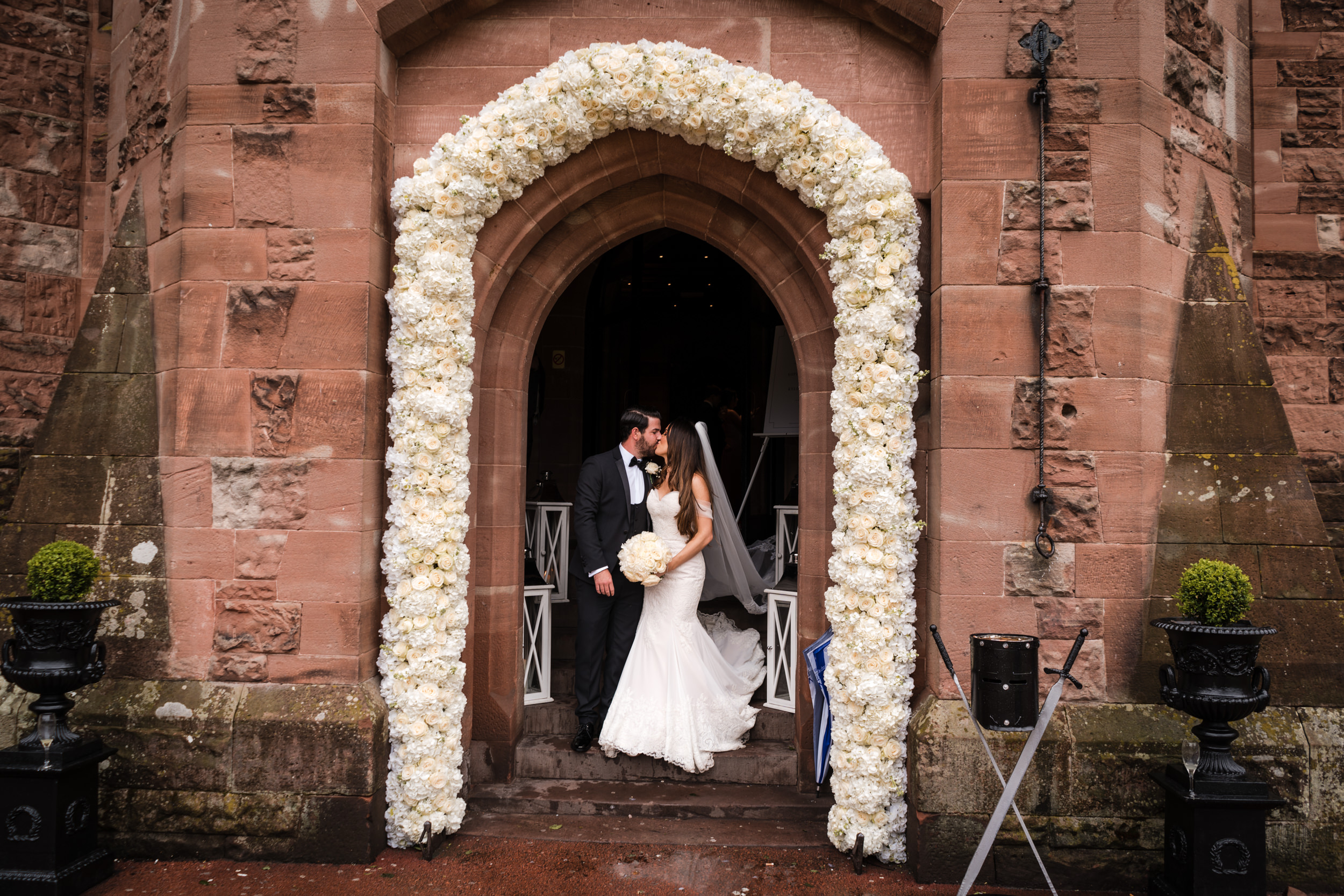Bride and groom kissing under their flower arch at Peckforton Castle