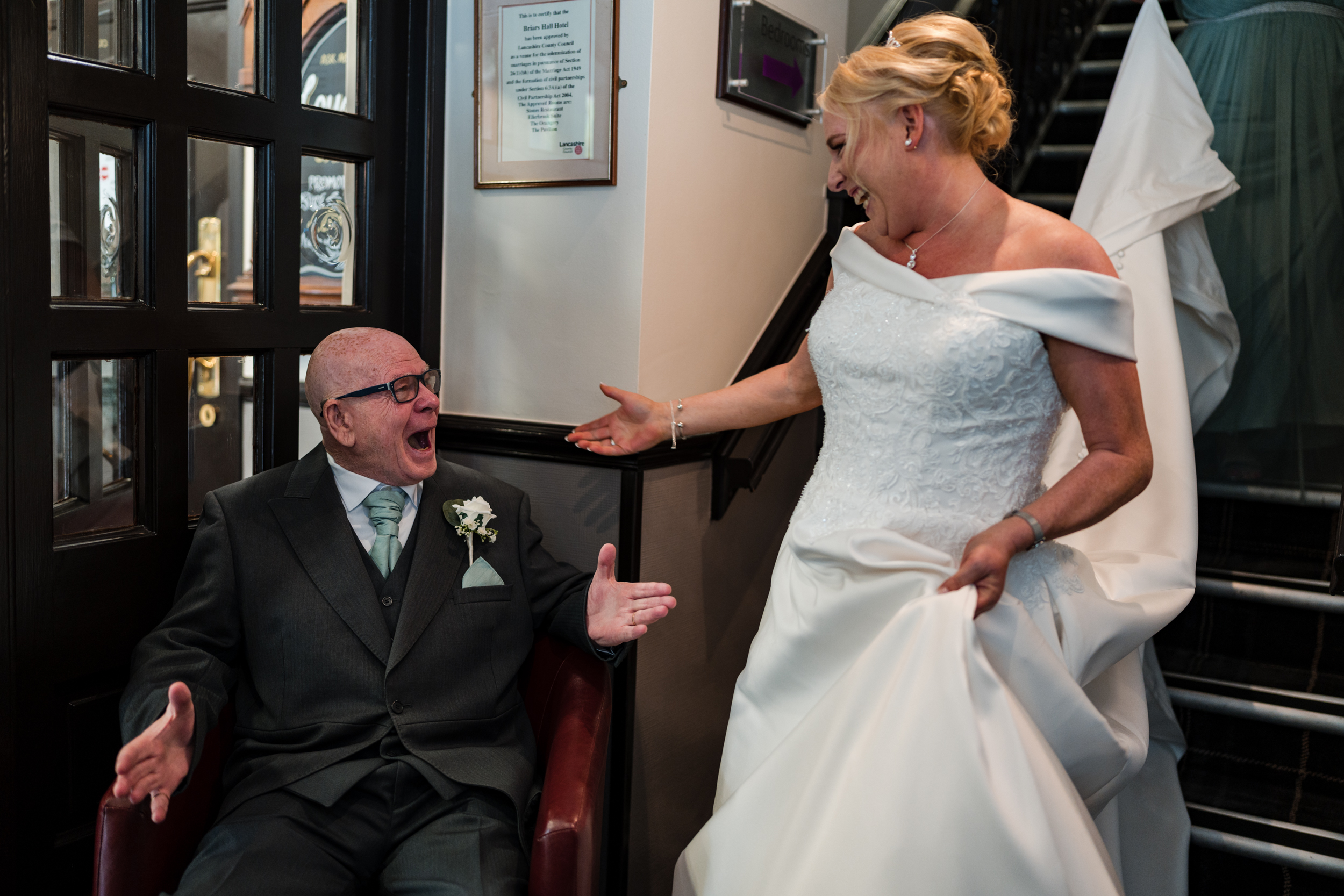 Bride showing her dad her dress at the bottom of the staircase at Briars Hall