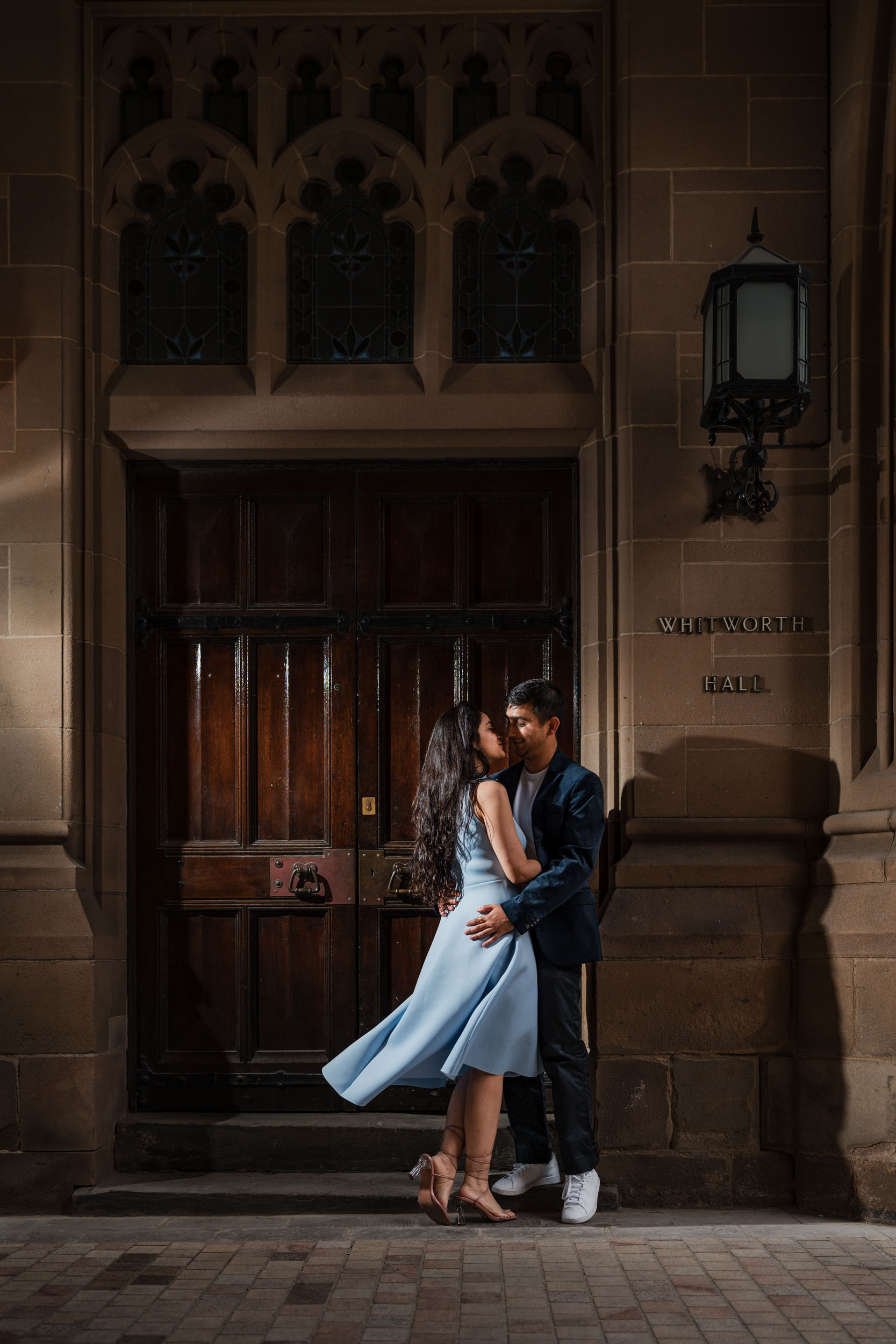 Lit portrait of the engaged couple in the Queen's Arch at the University of Manchester. 