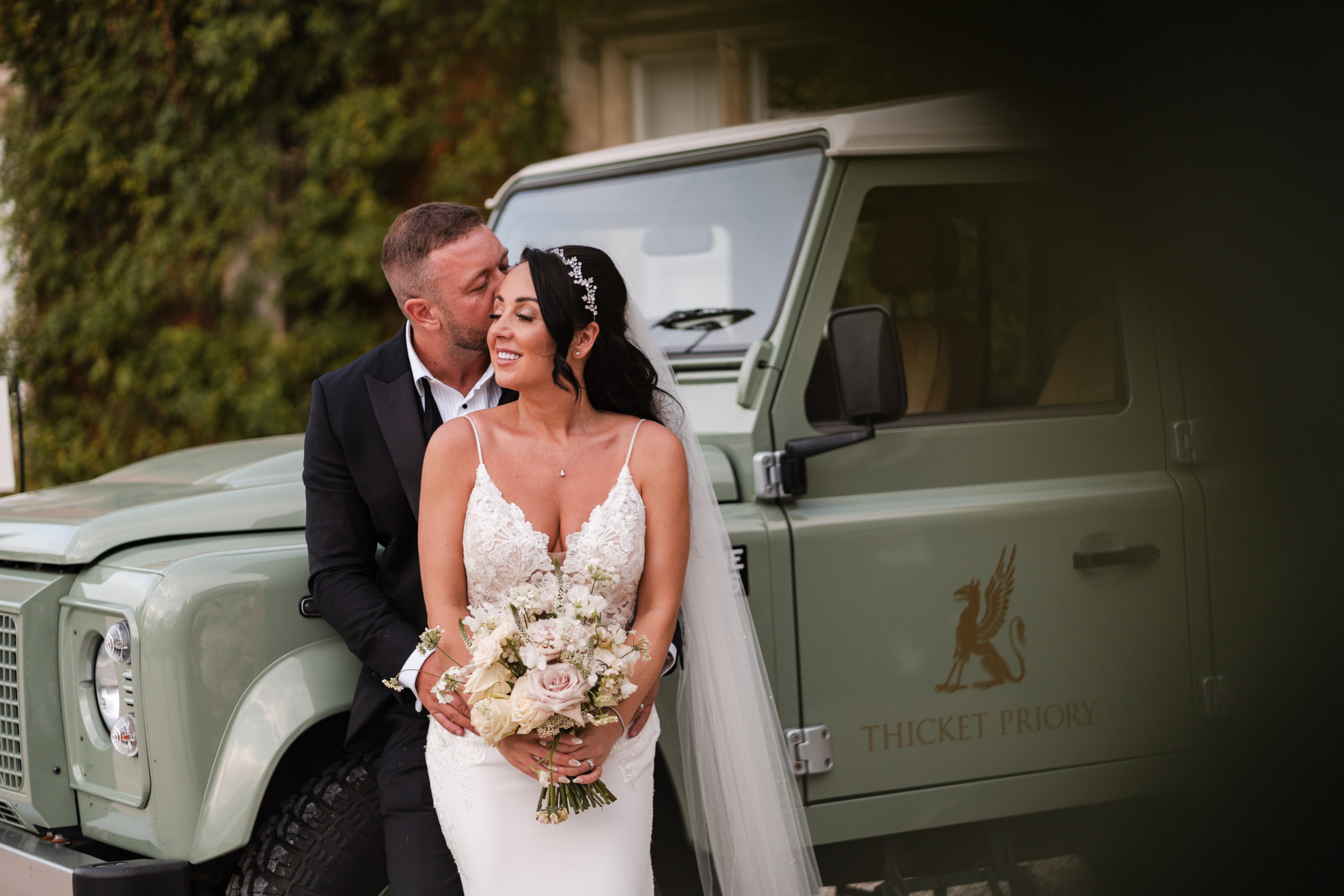 Bride and groom leaning on the land rover at Thicket Priory